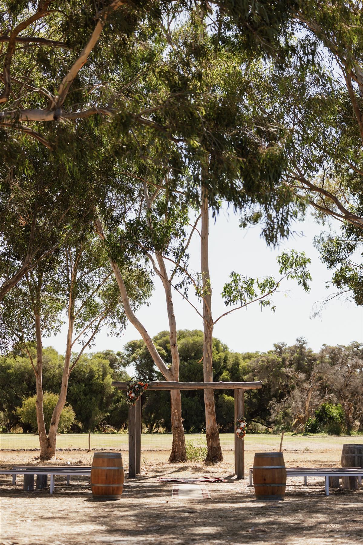 Rustic timber ceremony arbor with wine barrels and benches under gum trees